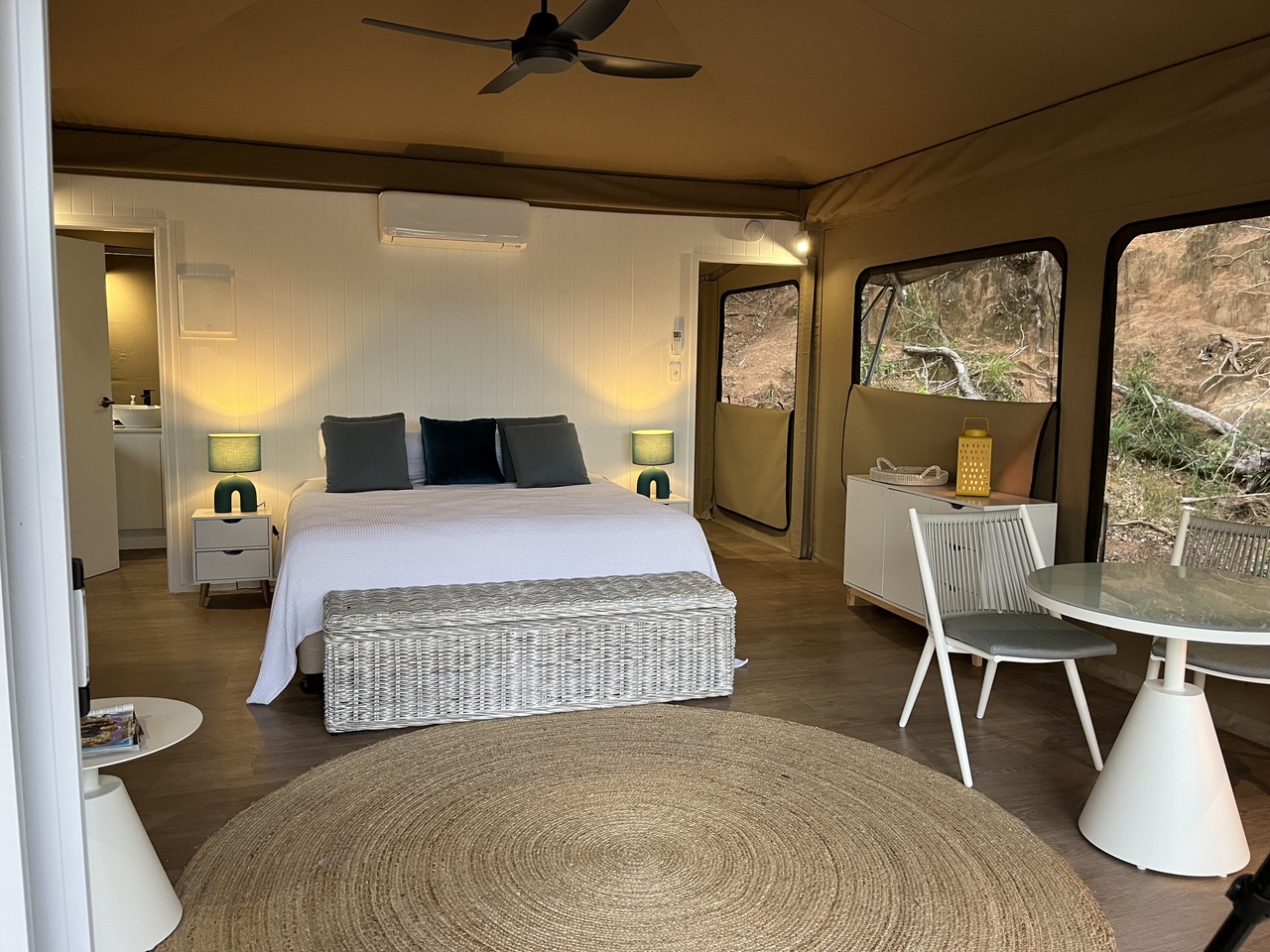 Inside a safari tent at Magnetic Glamping: king bed, ceiling fan, dining table and canvas windows onto the bushland