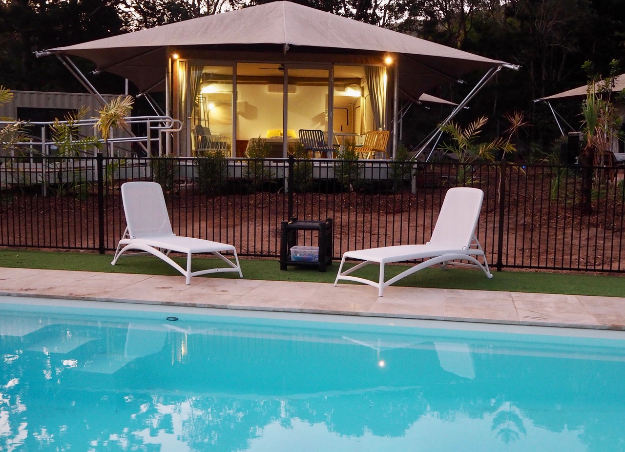 A safari tent glowing at dusk beyond the poolside sun loungers, Magnetic Glamping